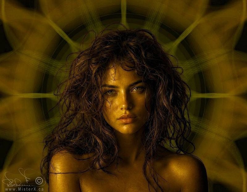 This ethereal digital portrait features a woman with a serene yet piercing gaze, framed by voluminous, textured brown curls that cascade over her bare shoulders. Her skin and hair are bathed in a warm, golden monochromatic light, giving her an almost metallic, statue-like appearance. In the background, a large, faint geometric mandala pattern creates a symmetrical halo effect around her head, softly radiating into the dark, olive-toned surroundings. The overall composition blends realism with a mystical, otherworldly aesthetic, highlighted by the soft play of shadows and the intense clarity of her light-colored eyes.